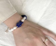 Handgjort armband med djupblå lapis lazuli, gyllene pyrit, vita sötvattenspärlor och en porslinsfisk. Justerbart med 3 cm förlän