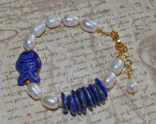 Handgjort armband med djupblå lapis lazuli, gyllene pyrit, vita sötvattenspärlor och en porslinsfisk. Justerbart med 3 cm förlän