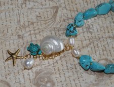 Handgjort halsband med turkosa howlit-nuggets, vita sötvattenspärlor och gyllene seed beads. Hänge med turbosnäcka, howlit-sköld