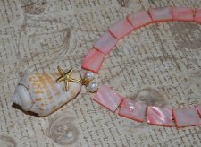 Handgjort halsband med korallrosa pärlemorpärlor, sötvattenspärlor och gyllene seed beads. Center med Alphabet Cone-snäcka och 1