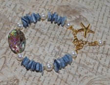 Mermaid-armband med vita sötvattenspärlor, havsblå snäckbitar och skimrande pauasnäcka i blågrön-lila ton. Dekorerat med 18K gul