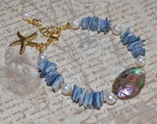 Mermaid-armband med vita sötvattenspärlor, havsblå snäckbitar och skimrande pauasnäcka i blågrön-lila ton. Dekorerat med 18K gul