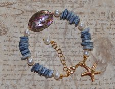 Mermaid-armband med vita sötvattenspärlor, havsblå snäckbitar och skimrande pauasnäcka i blågrön-lila ton. Dekorerat med 18K gul