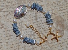 Mermaid-armband med vita sötvattenspärlor, havsblå snäckbitar och skimrande pauasnäcka i blågrön-lila ton. Dekorerat med 18K gul
