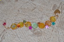 Färgglatt Y2K-armband med pärlemorsmynt i gul, orange och grön, samt flerfärgade pärlemorsstjärnor. Dekorerat med 18K guldpläter