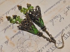 Handgjorda örhängen i Fairycore-stil med bronsfärgade filigranblommor och polerade peridotpärlor som glimmar i grönt. De svängan