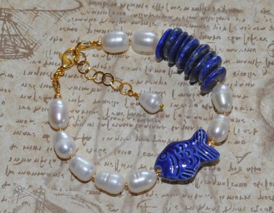 Handgjort armband med djupblå lapis lazuli, gyllene pyrit, vita sötvattenspärlor och en porslinsfisk. Justerbart med 3 cm förlän