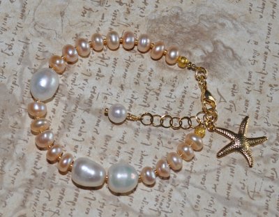 Handgjort armband med vita och persikofärgade sötvattenspärlor, dekorerat med 18K guldförgyllt sjöstjärnehänge. Perfekt för merm