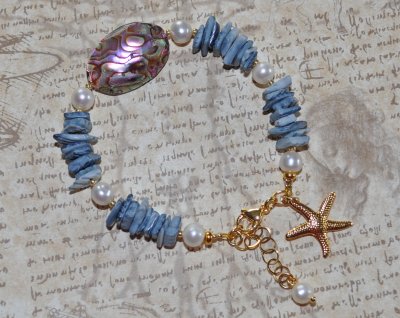 Mermaid-armband med vita sötvattenspärlor, havsblå snäckbitar och skimrande pauasnäcka i blågrön-lila ton. Dekorerat med 18K gul